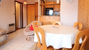 A dining area with a round table, wooden chairs, a bench, and a kitchen in the background. - 3 Rooms in Carroz, 6 Pers, Terrace, Parking (Les Carroz d'Arâches)
