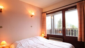 A bedroom with a large bed, two wall-mounted lamps, a window with curtains, and a view of a balcony. - 3 Rooms in Carroz, 6 Pers, Terrace, Parking (Les Carroz d'Arâches)