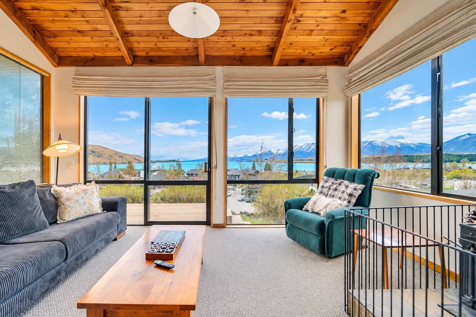 A room with a wooden ceiling, a sofa, a green armchair, a coffee table, and large windows offering a mountain view.