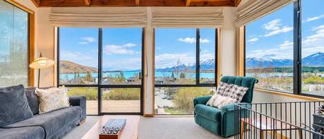 Una habitación con techo de madera, un sofá, un sillón verde, una mesa de centro y ventanas amplias con vistas a la montaña.