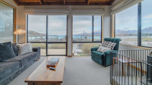 Un salon moderne avec un canapé, un fauteuil et une table basse, de grandes fenêtres offrant une vue sur les montagnes.