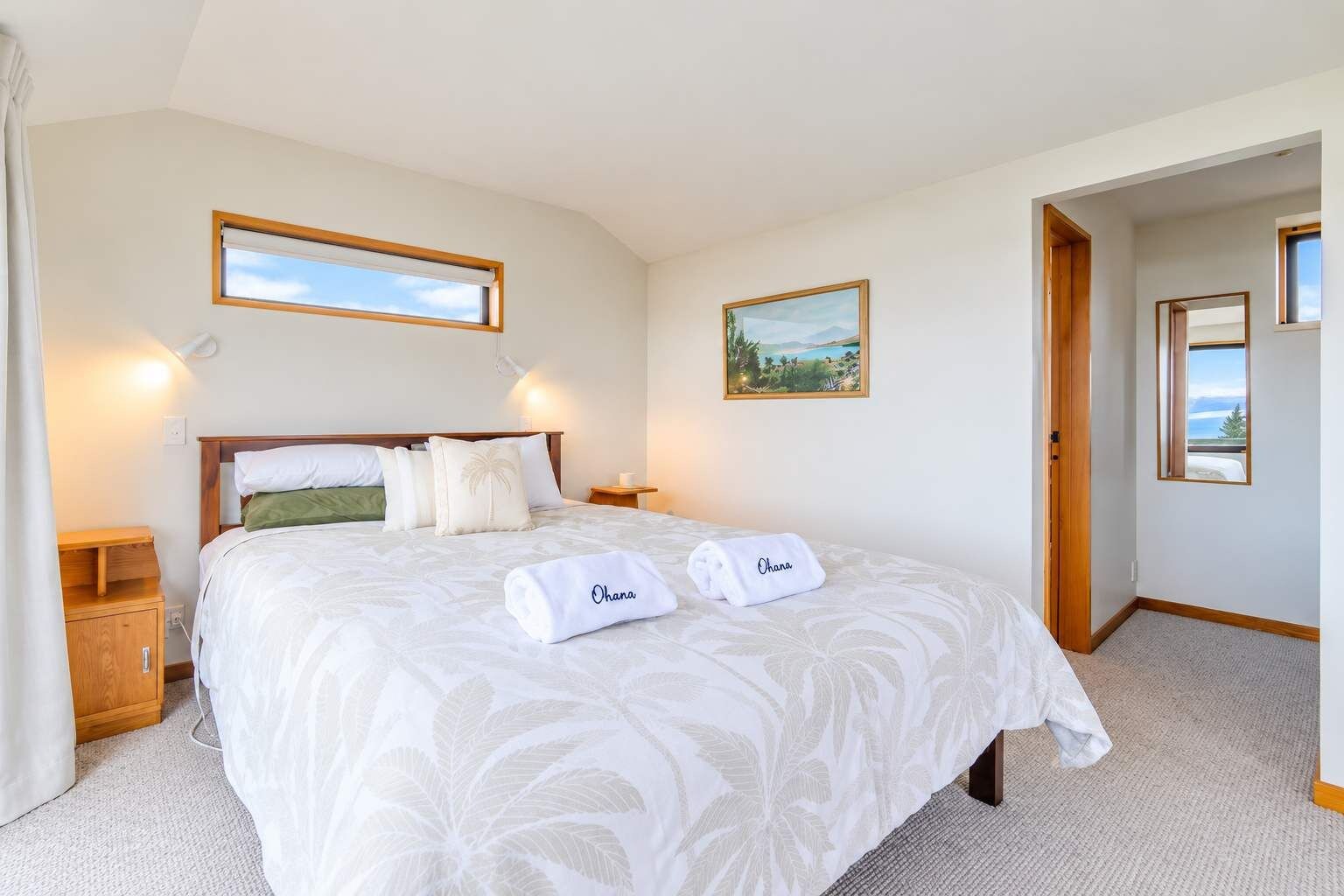 Een hotelkamer met een groot bed, twee nachtkastjes, een wandeling en een deur naar een andere kamer.