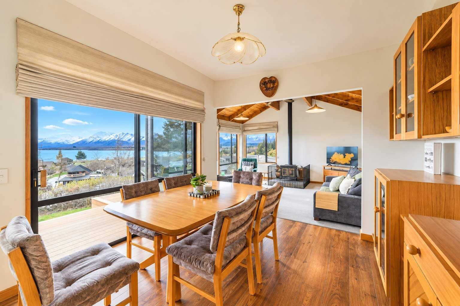 A spacious living area with a wooden dining table, comfortable seating, a fireplace, and large windows offering a mountain view.