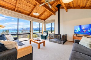 Ein geräumiges Wohnzimmer mit großem Fernseher, Holzboden und Blick auf Berge durch große Fenster.