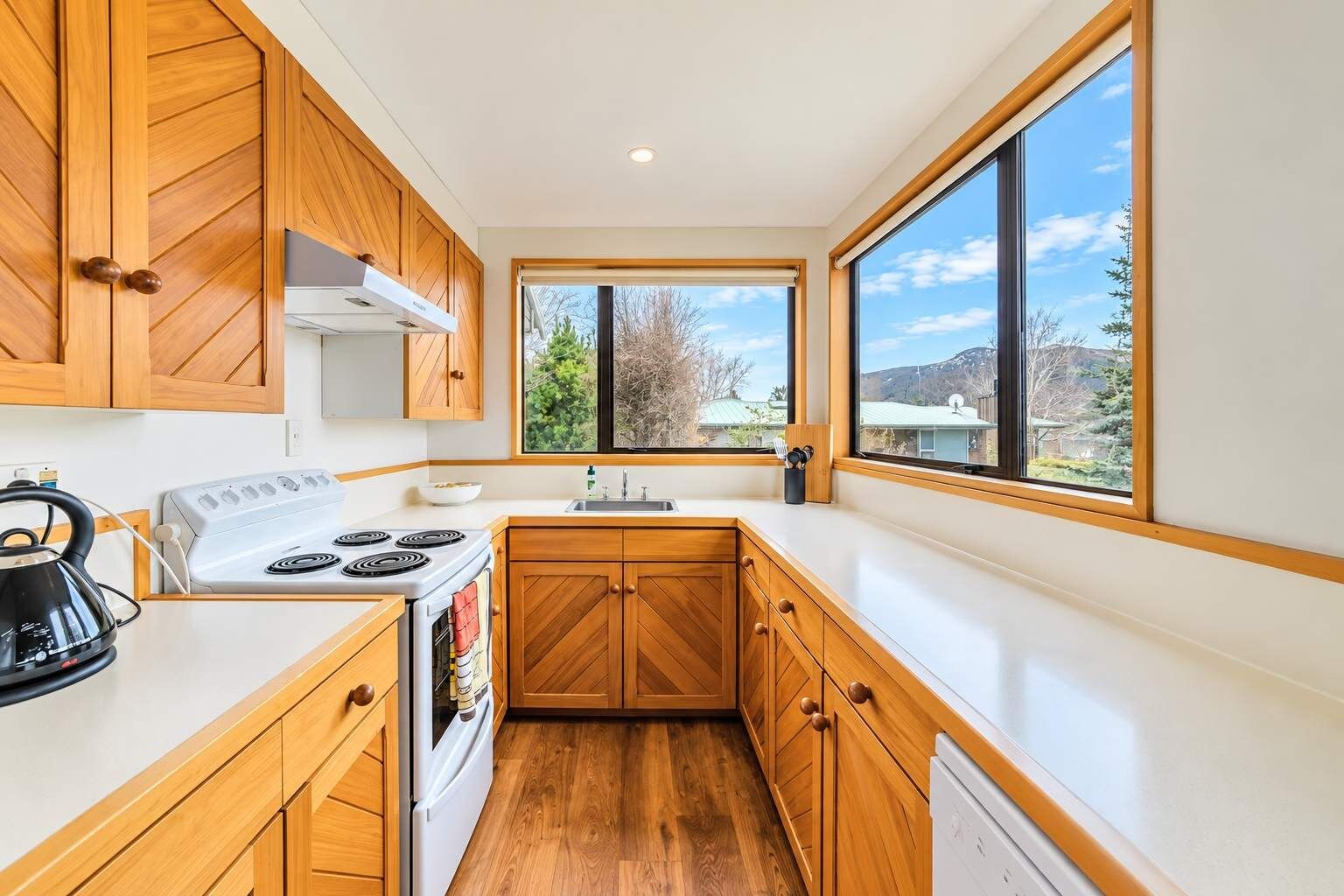 A modern kitchen with wooden cabinets, a stove, and a large window offering a view of the outdoors.