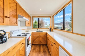 Een moderne keuken met houten kastjes, een fornuis en een groot raam met uitzicht op het landschap.