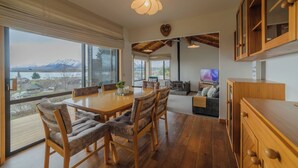 Un vaste espace de vie comprenant une table à manger en bois, des sièges confortables, une cheminée et une grande fenêtre donnant sur les montagnes.