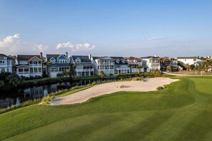 Um campo de golfe com um lago, um bunker de areia e uma fileira de casas com cerca.