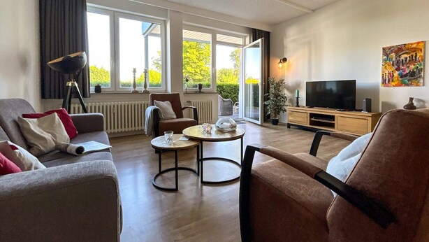 Una sala de estar moderna con un sofá, sillones, una mesa de centro y un televisor.