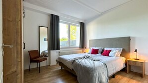 Un dormitorio moderno con una cama grande, una silla, una mesita de noche y una ventana con cortinas.