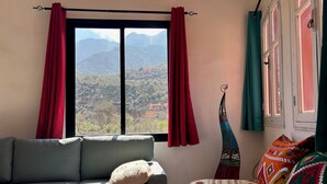 A room with a sofa and a bed, a window with curtains, and a view of mountains. - Chez Yahia, in the heart of Ourika, apartment with panoramic view (Ourika)