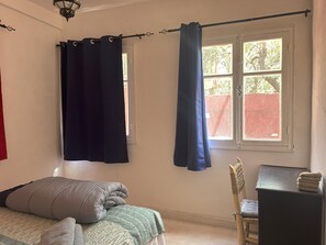A bedroom with a bed, a chair, a desk, and a window with curtains.