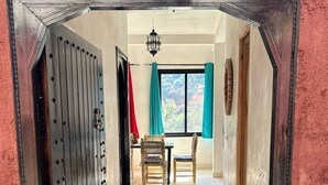 A hallway with a metal door, a dining area with chairs and a table, and a view of the outside through a window. - Chez Yahia, in the heart of Ourika, apartment with panoramic view (Ourika)