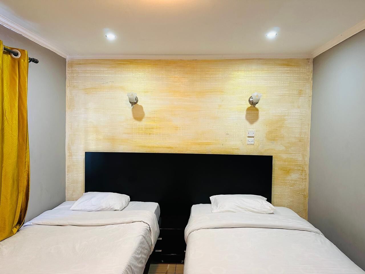 Une chambre avec deux lits, une tête de lit en bois et deux lampes fixées au mur.