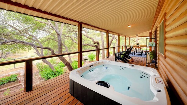 Een hottub op een houten terras met een overdekte ruimte, omringd door bomen.