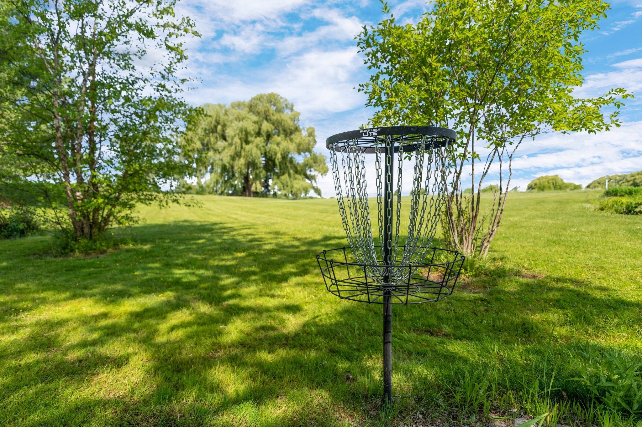 A disc golf basket in a grassy field with trees in the background.