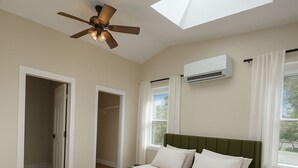Un dormitorio con cama, ventilador de techo, tragaluces, equipo de aire acondicionado y ventana con cortinas.