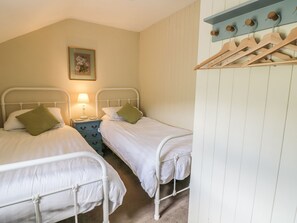 Ein Schlafzimmer mit zwei Einzelbetten, einem Nachttisch mit Lampe, einem Holz-Kleiderständer und einem gerahmten Bild an der Wand.