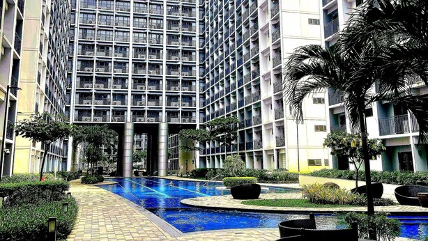 Un moderno edificio de gran altura con un patio central que tiene una piscina, rodeado de vegetación y zonas de estar al aire libre.