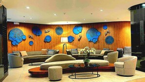 Un vestíbulo moderno con techo curvo, una pared de madera con patrones circulares azules, un conjunto de sofás y una mesa de centro con un florero.