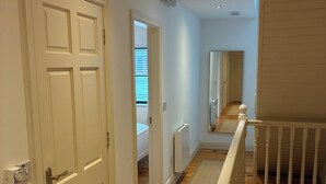 A hallway with white doors, a wooden floor, a white railing, and a radiator.