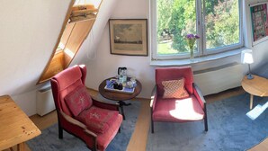 A room with a red armchair, a small round table with a lamp, a window with a view of greenery, and a bed with a blue mattress. - Vacation apartment near Volkspark, arenas / Trabrennbahn /DESY (Hamburg)