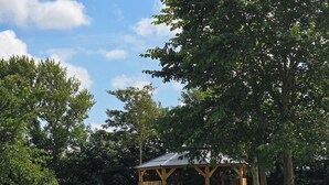 A wooden gazebo with a sloped roof, surrounded by lush green grass and trees. - Vacation apartment "Sandra" in Denmark  (Bredebro)