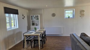 A dining area with a table and chairs, a white cabinet, a clock, and a window with a view of greenery. - Vacation apartment "Sandra" in Denmark  (Bredebro)