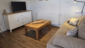A living room with a wooden coffee table, a sofa, a TV on a wooden shelf, and a radiator. - Vacation apartment "Sandra" in Denmark  (Bredebro)