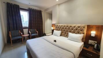 Une chambre d’hôtel avec un grand lit, deux chaises, une table de chevet avec une lampe et une fenêtre avec des rideaux.