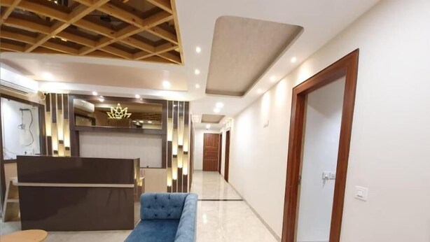 A modern hotel lobby with a reception desk, a blue sofa, and a wooden ceiling structure. - Hotel Scarlet (Gwalior)