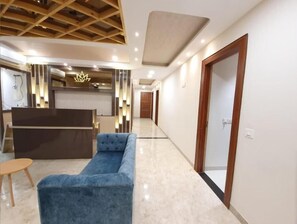 A modern hotel lobby with a reception desk, a blue sofa, and a wooden ceiling structure. - Hotel Scarlet (Gwalior)
