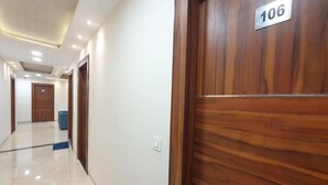 A hallway with a wooden door labeled 106, a blue trash bin, and a white wall. - Hotel Scarlet (Gwalior)