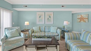 Un salon avec un canapé à rayures, une table basse et un fauteuil. On y trouve deux cadres photos accroch és au mur et une décoration en forme d’étoile de mer.
