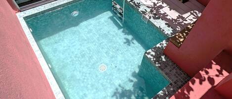 A small, rectangular swimming pool with a tiled edge, a metal ladder, and a drain in the center.