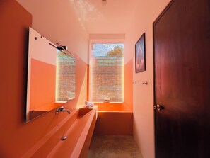 Une salle de bain avec un grand miroir, un lavabo et une fenêtre avec des stores.