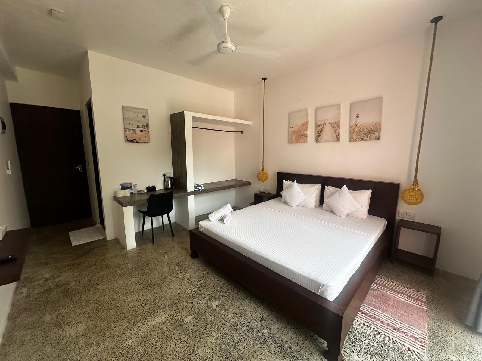 Ein Hotelzimmer mit einem großen Bett, einem Schreibtisch, einem Sessel, einem Kleiderschrank und einem Deckenventilator.