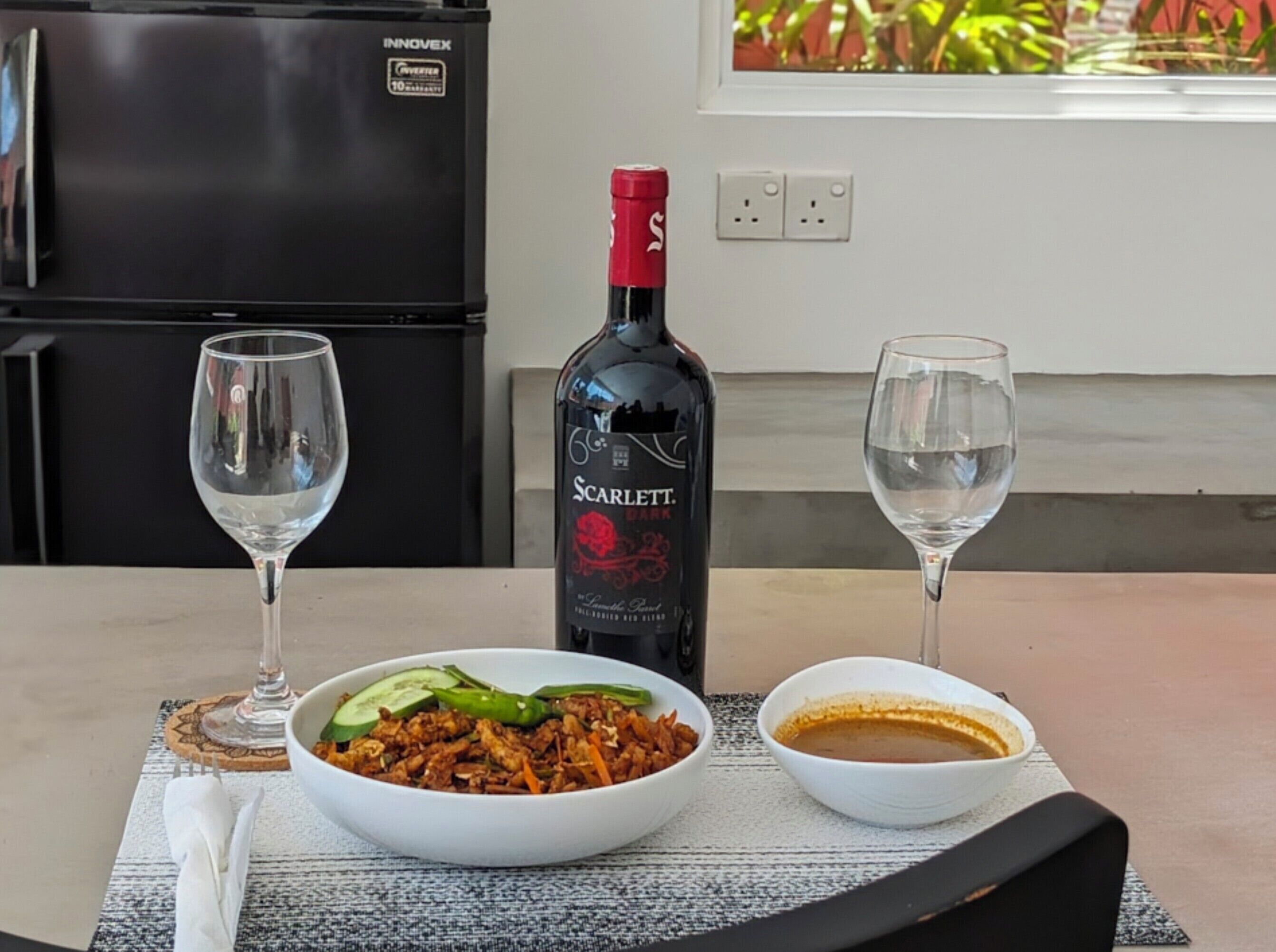 A dining table with a bottle of Scarlett wine, two glasses, and a bowl of food.