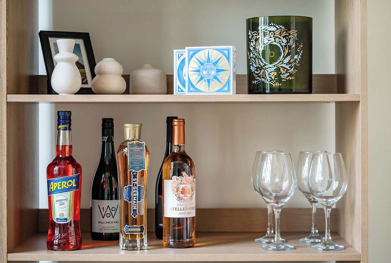 Uma prateleira com diversos frascos e copos, incluindo Aperol, St. Germain e Willunga 100.