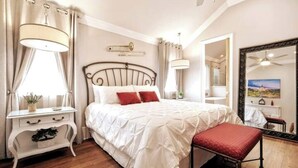 Un dormitorio con una cama grande, una mesita de noche con lámpara, un espejo y una ventana con cortinas.
