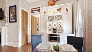 Una cocina moderna con armarios blancos, horno empotrado y cafetera. Hay una mesa de comedor con sillas y una planta en maceta.