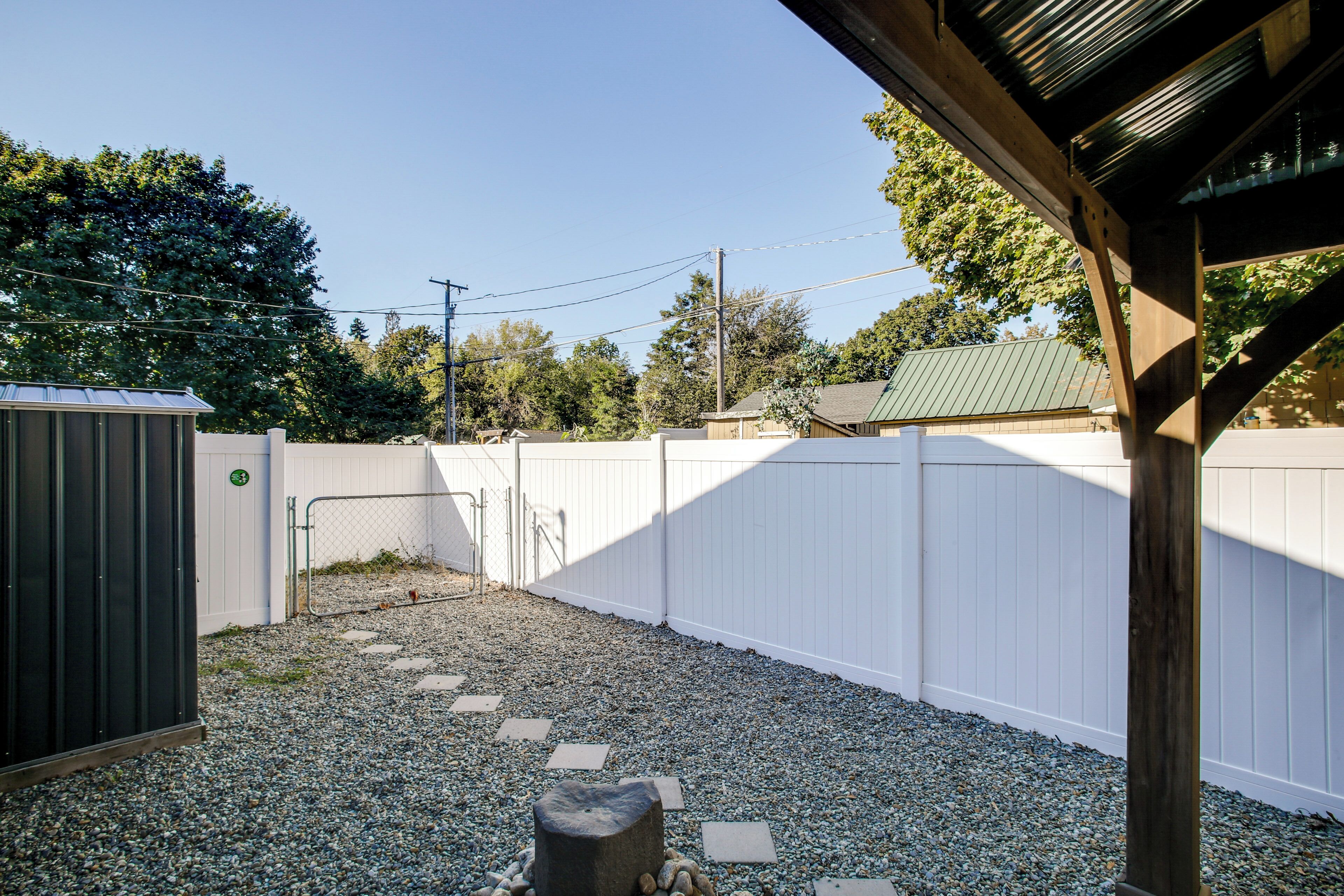 A backyard with a white fence, gravel path, and a wooden structure.