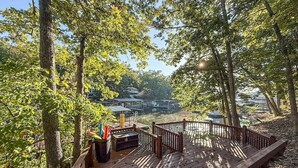 Une terrasse en bois, dotée d’une rambarde, entourée d’arbres et offrant une vue sur une étendue d’eau où se trouvent des bateaux.