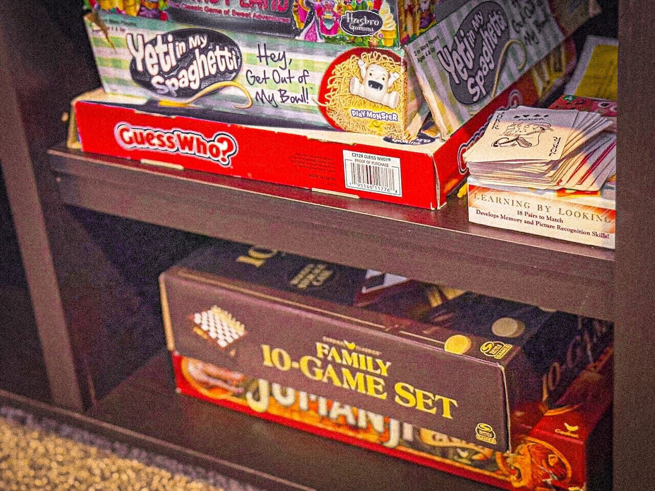 Ein Regal mit verschiedenen Gesellschaftsspielen, darunter 'Guess Who?', 'Yetis in My Spaghetti' und 'Family Game Set'.