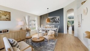 Sala de estar moderna com área de jantar, piso de madeira e uma janela grande com persianas.