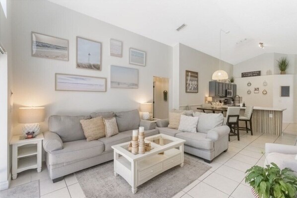 A modern living room with a grey sofa, a white coffee table, and a kitchen area in the background.