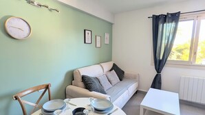 Ein Essbereich mit einem runden Tisch für vier Personen, einer Couch, einem kleinen weißen Tisch und einem Fenster mit Vorhängen.