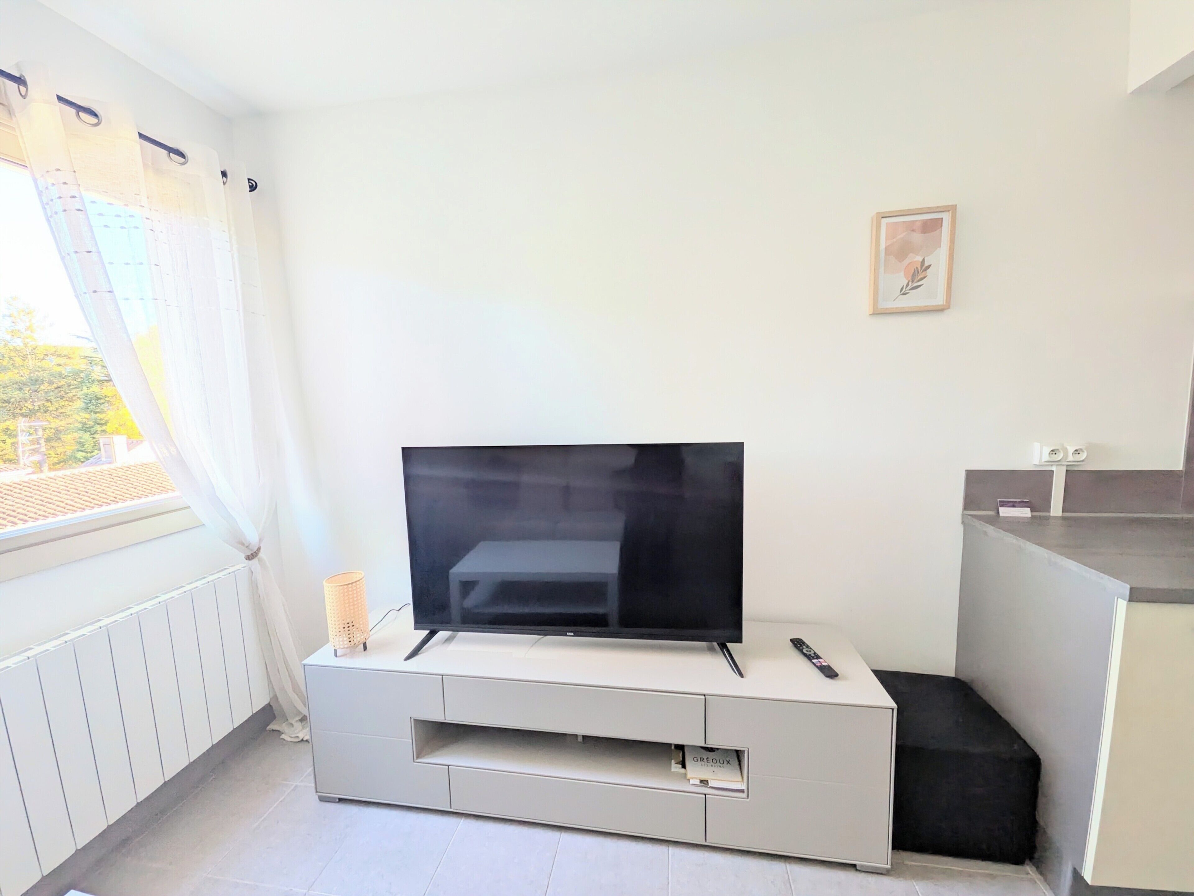 Ein modernes Wohnzimmer mit einem Flachbildfernseher auf einer weißen Unterhaltungseinheit, einer Fernbedienung auf der Einheit und einem gerahmten Bild an der Wand.