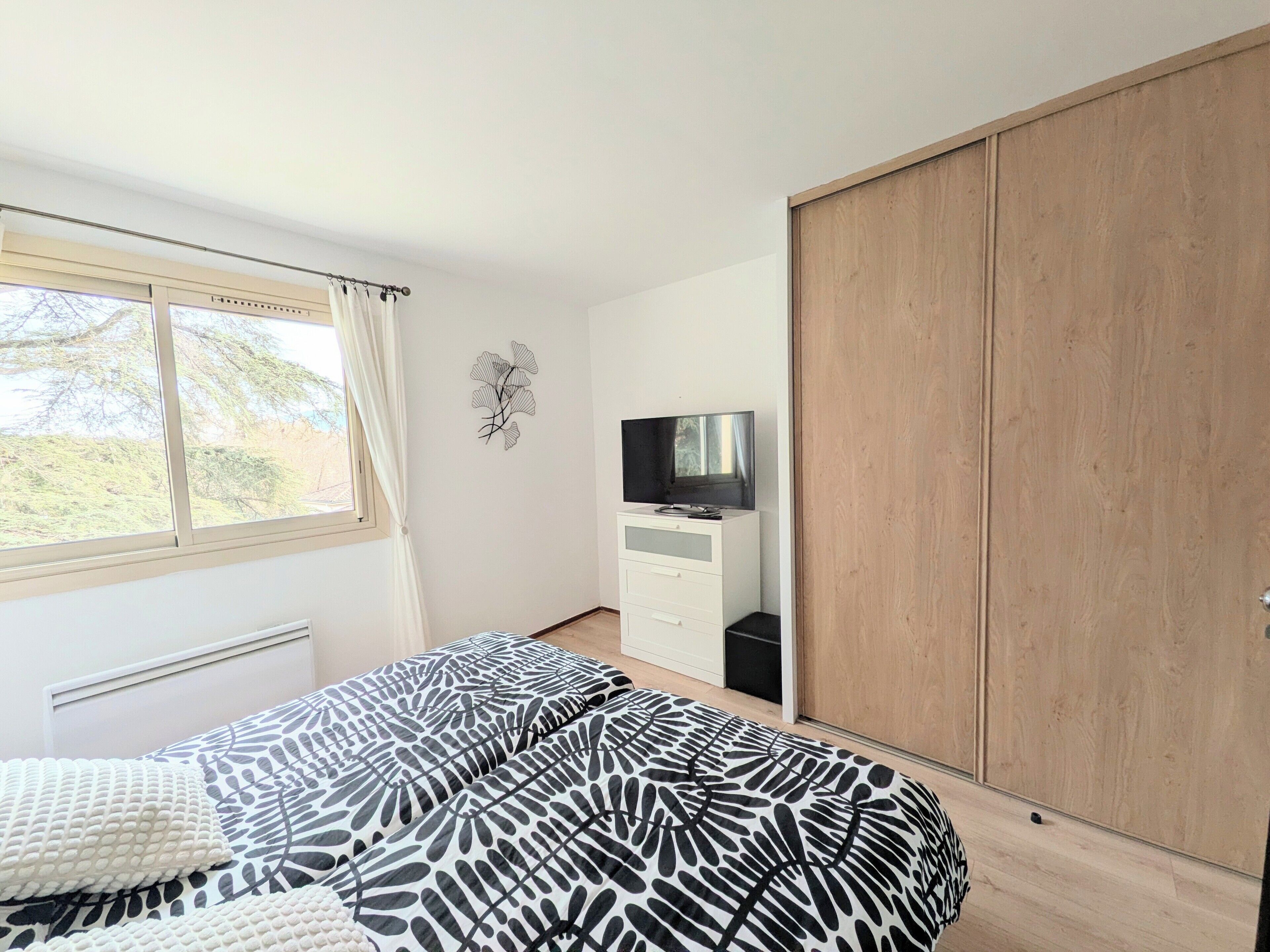 A bedroom with a bed, a TV, a wardrobe, and a window with curtains.