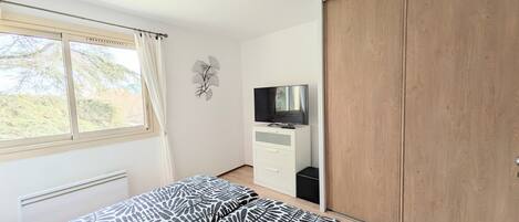A bedroom with a bed, a TV, a wardrobe, and a window with curtains.